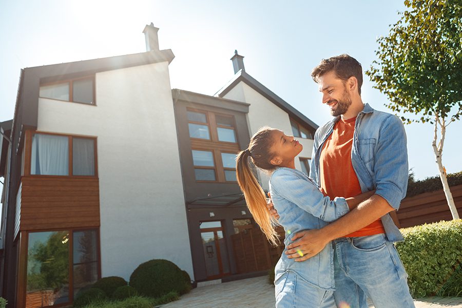 Personal Insurance - Young Couple Standing in Front of New House Together at Dusk